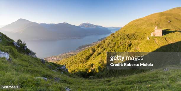 sun on church of san bernardo lights up the landscape around the blue water of lake como at dawn, musso, lombardy, italy, europe - san bernardo stock pictures, royalty-free photos & images