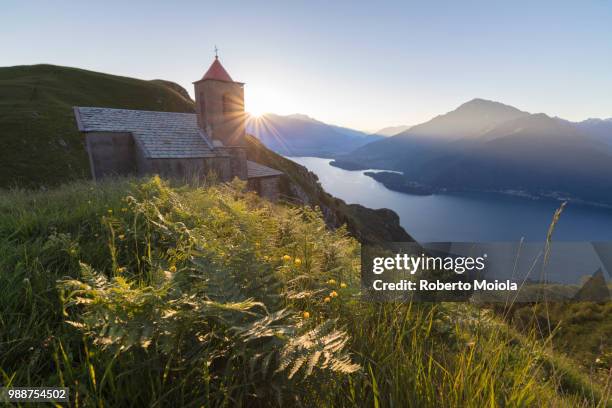 sunbeam on church of san bernardo lights up the landscape around the blue water of lake como at dawn, musso, lombardy, italy, europe - san bernardo stock pictures, royalty-free photos & images