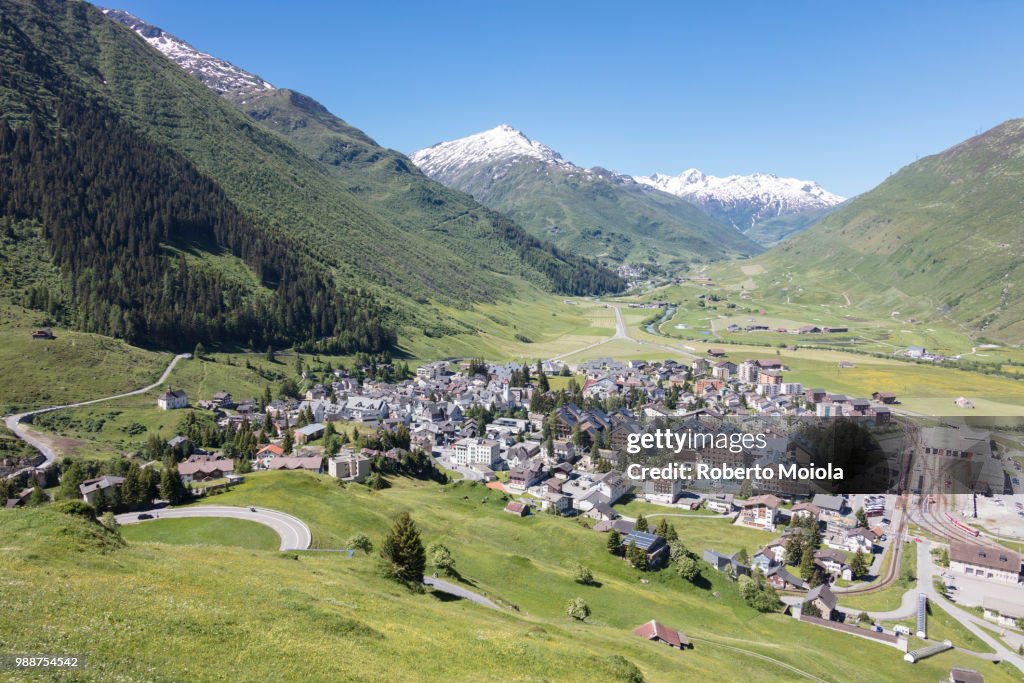 The alpine village of Andermatt surrounded by green meadows, and snowy peaks in the background, Canton of Uri, Switzerland, Europe