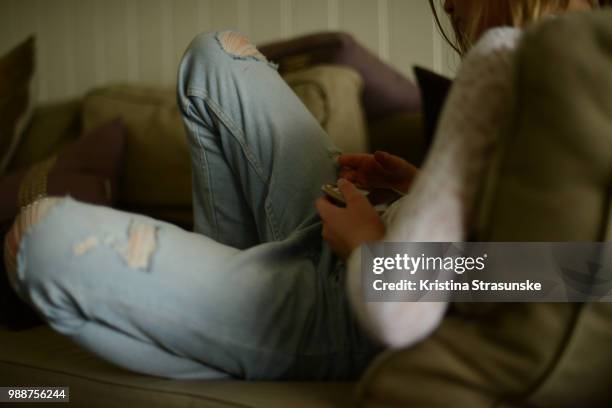 a girl sitting on a coach relaxing with her mobile phone - kristina strasunske ストックフォトと画像