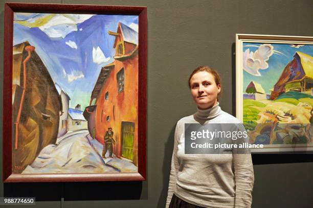 Curator Liis Paehlapuu stands next to the paintings 'Tallinna taenav' and 'Mulgi talu' by Peet Aren at the exhibition 'The Savages of Germany. Die...