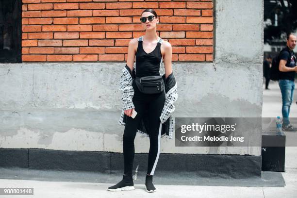 Model Dina Parpalia wears a black body suit, white patterned jacket off her shoulders, black fanny pack, black and white pants, and black Balenciaga...