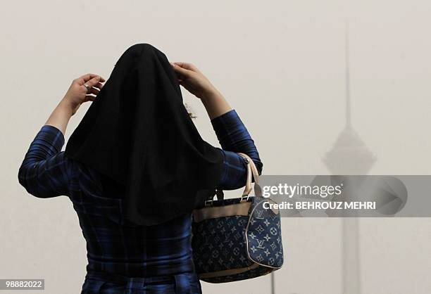 An Iranian woman adjusts her headscarf as smog covers the Milad telecommunications tower in northwestern Tehran on July 7, 2009. Iranian opposition...