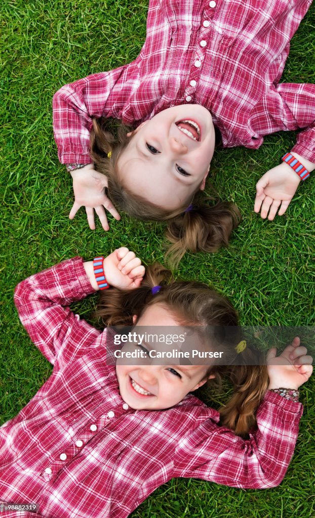 Twin girls lying on grass looking up and smiling