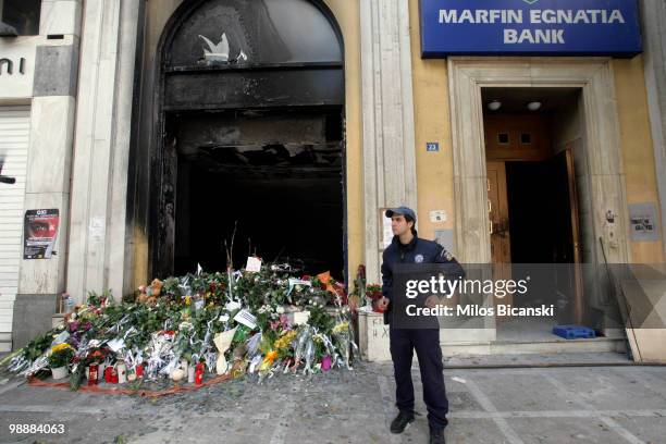 Policeman stands guard next to flowers laid in rememberance outside a bank where three people were killed in protests on May 6, 2010 in Athens. Three...