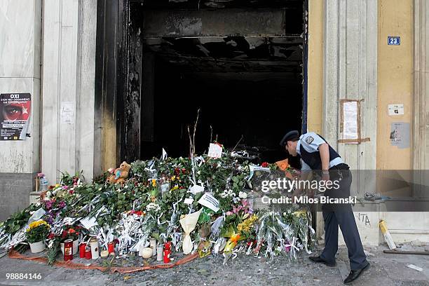 Policeman looks at flowers laid in rememberance outside a bank where three people were killed in protests on May 6, 2010 in Athens. Three people, one...