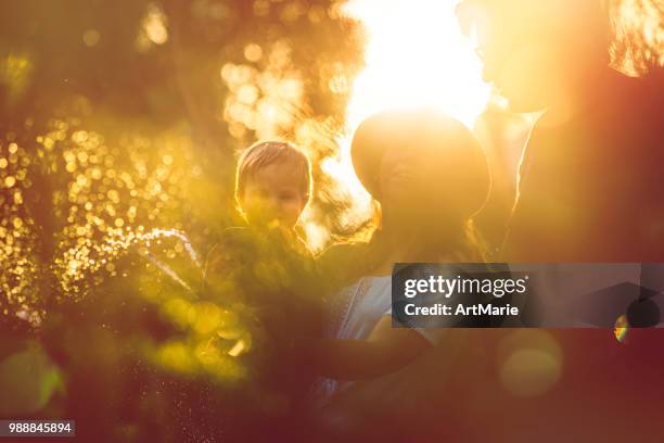 family in the garden in sunset - artmarie stock pictures, royalty-free photos & images