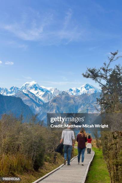 tourists take a scenic hike in lake matheson. the famous fox glacier is seen in the distance. - lake matheson foto e immagini stock