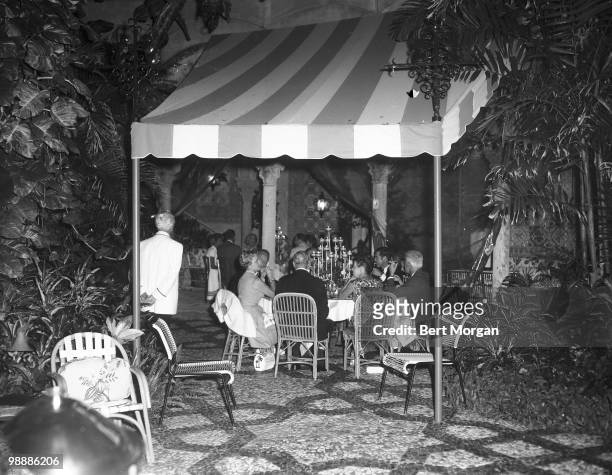 View of unidentified guests under a striped awning on the tiled garden terrace at Mar-a-Lago , Palm Beach, Florida, mid 1950s. The residence,...
