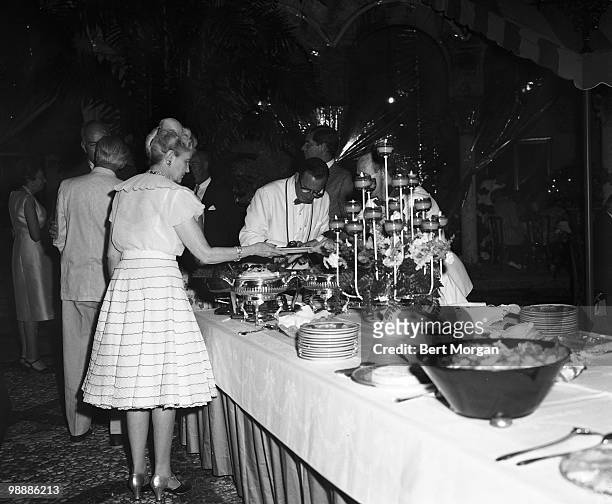 American heiress, businesswoman, and philanthropist Marjorie Merriweather Post fills her plate during a buffet-style meal at a party on the tiled...