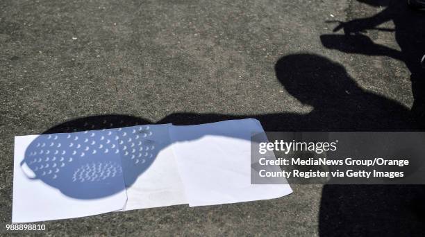 Computer teacher Russ Day holds a kitchen colander as the round holds show the shape of the partial solar eclipse at Lexington Junior High School in...