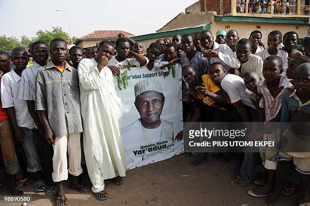 People stand by the poster of late Nigerian President Umaru Musa Yar'Adua at Katsina stadium before his burial in Katsina on May 6, 2010. Thousands...