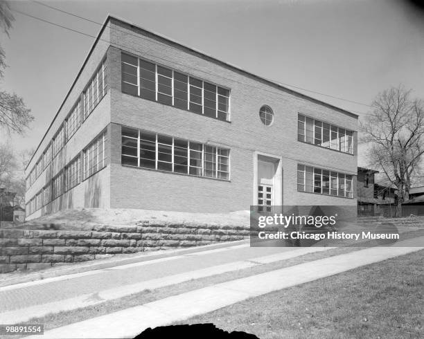 Exterior view of the Industrial Arts School, a two-story brick building with ribbon windows, showing the narrow end of the building with a doorway....