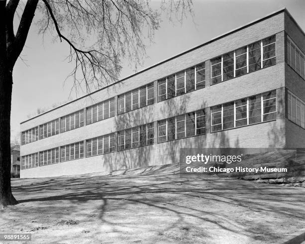 Exterior view of the Industrial Arts School, a two-story brick building with ribbon windows, showing the back of the building with two long rows of...