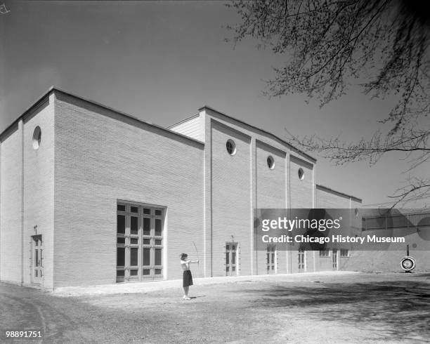 Exterior view of the Clark Field House, located at 919 Market Street in Burlington, IA, 1940. A girl in an archery outfit shoots at a target; the...