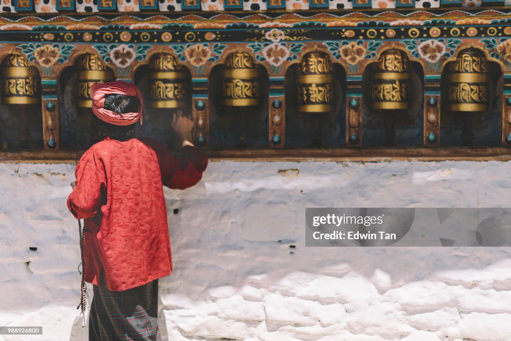 An old bhutanese female at the temple praying at prayer wheel