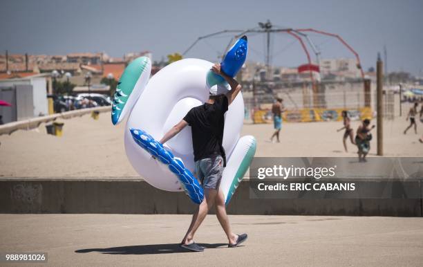 Man holds a rubber ring as he walks along the sea-front in Narbonne on July 1, 2018.