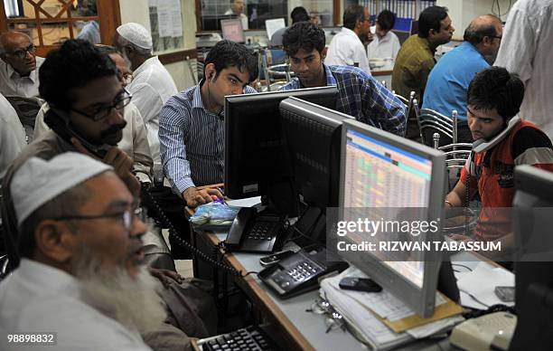 Pakistani stock dealers talk on phone while they watch the latest share prices at a brokerage house during a trading session in Karachi on May 7,...