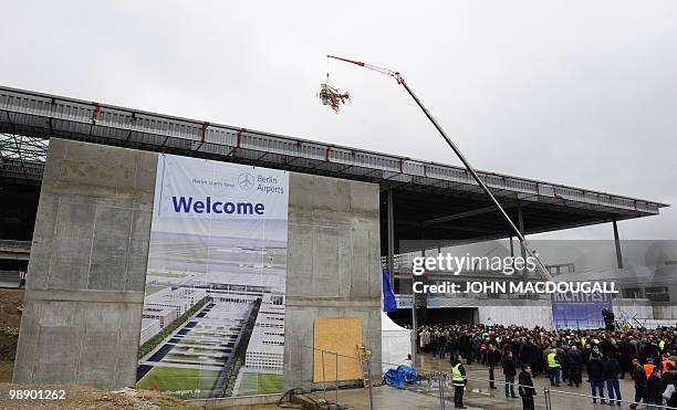 An airplane shaped crown is lifted by a crane over the main terminal of the Berlin-Brandenburg International airport during a traditional "topping...