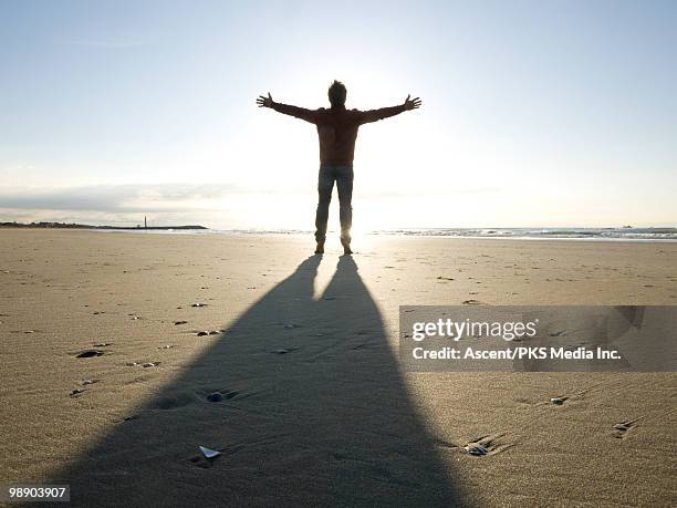 man stands on beach, arms outstretched - shade45 stock pictures, royalty-free photos & images