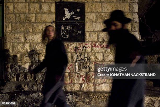 Ultra-Orthodox Jewish men walk past graffiti after praying at the tomb of the biblical Israeli leader Yehoshua bin Nun in the northern Palestinian...
