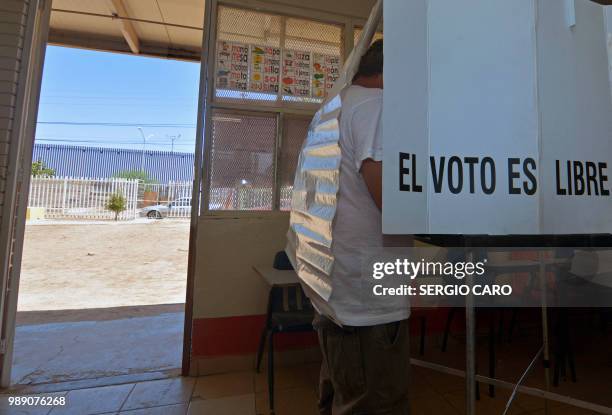 Man casts his vote at a polling station as the US-Mexico border fence is seen on the background, in Mexicali on July 1, 2018. Fed up with corruption...