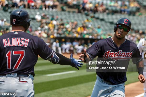 Michael Brantley of the Cleveland Indians is congratulated by Yonder Alonso after scoring a run against the Oakland Athletics during the first inning...
