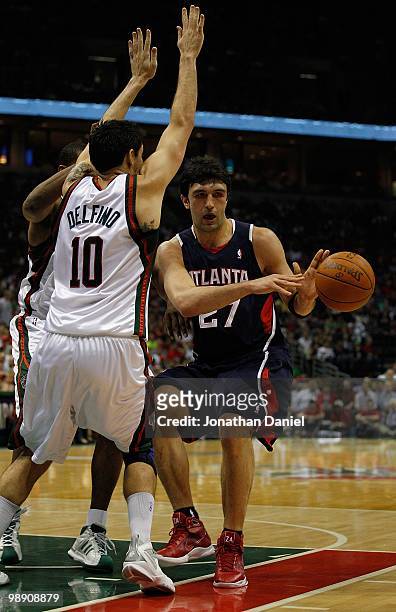 Zaza Pachulia of the Atlanta Hawks passes the ball under pressure from Carlos Delfino of the Milwaukee Bucks in Game Six of the Eastern Conference...