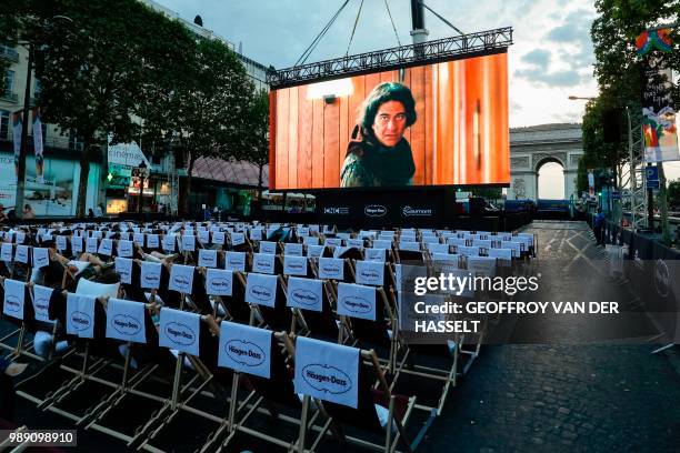 People watch a movie on a giant screen during the "Un dimanche au cinema" outdoor cinema event on the Champs Elysees avenue in front of the Arc de...