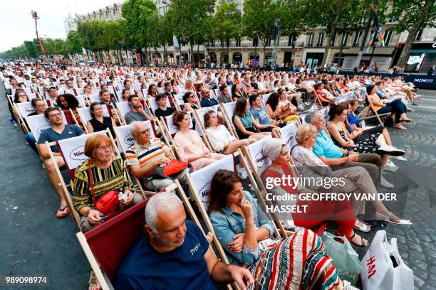 People watch a movie on a giant screen during the "Un dimanche au cinema" outdoor cinema event on the Champs Elysees avenue in front of the Arc de...