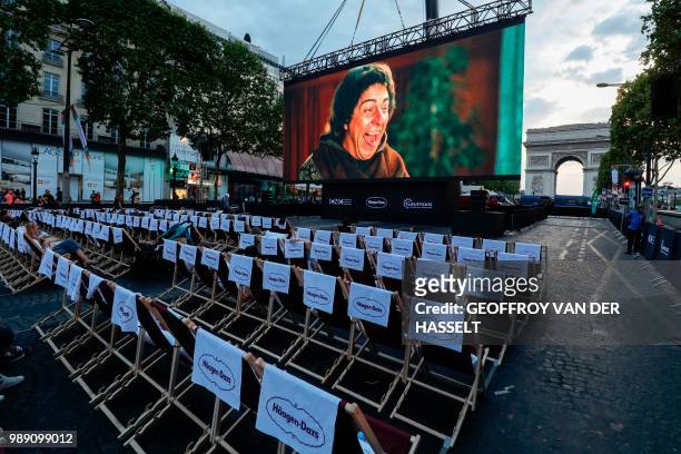 People watch a movie on a giant screen during the "Un dimanche au cinema" outdoor cinema event on the Champs Elysees avenue in front of the Arc de...