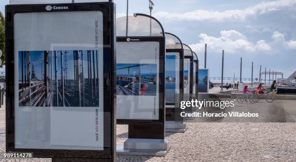 Children cycle past pictures from the open air photo exhibition "Voce Nao Esta Aqui" by Portuguese photojournalist Bruno Portela depicting the area...