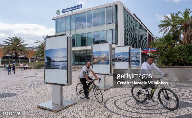 Cyclists ride by pictures from the open air photo exhibition "Voce Nao Esta Aqui" by Portuguese photojournalist Bruno Portela depicting the area as...