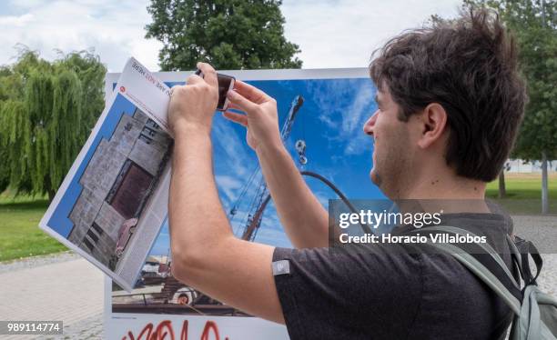 Visitor takes a picture while holding the catalog of the open air photo exhibition "Voce Nao Esta Aqui" by Portuguese photojournalist Bruno Portela,...