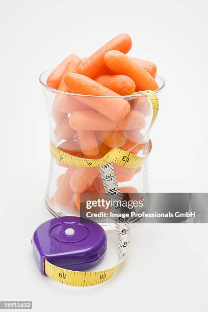 baby carrots in glass with tape measure around it - ベビーキャロット ストックフォトと画像