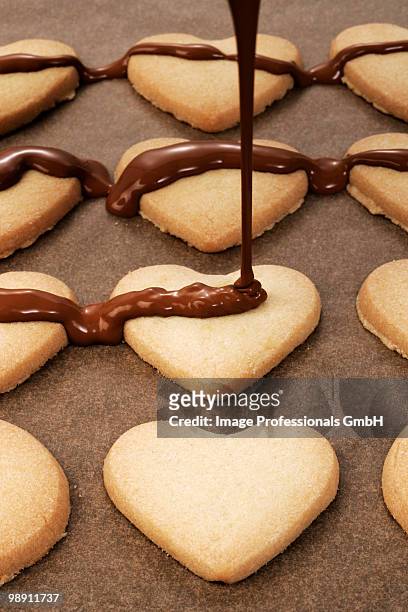 pouring couverture chocolate on heart shaped biscuits, close-up - couverture stock pictures, royalty-free photos & images