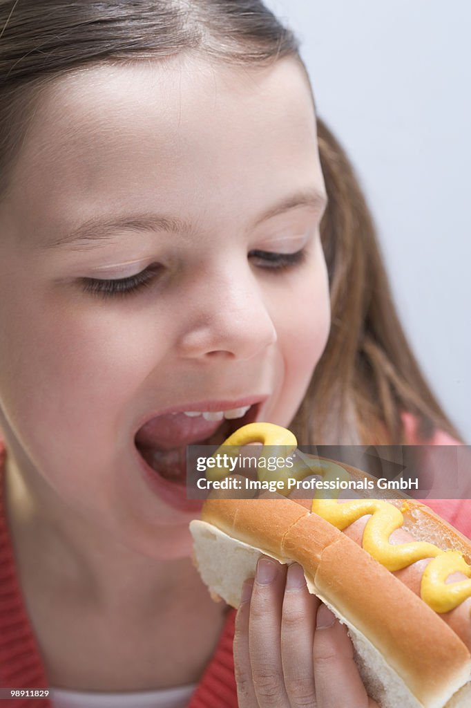 Girl (6-7) eating hot dog with mustard, close-up