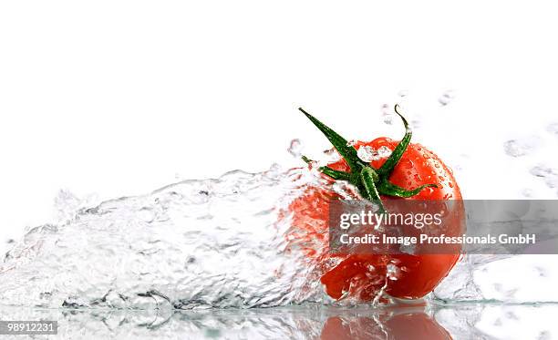 tomato with splashing water, close-up - kelkblaadje stockfoto's en -beelden