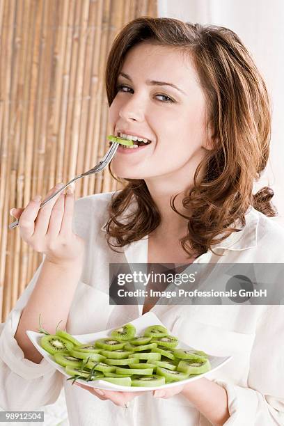 young woman eating kiwi fruit, portrait, close-up - vierkant bord stockfoto's en -beelden