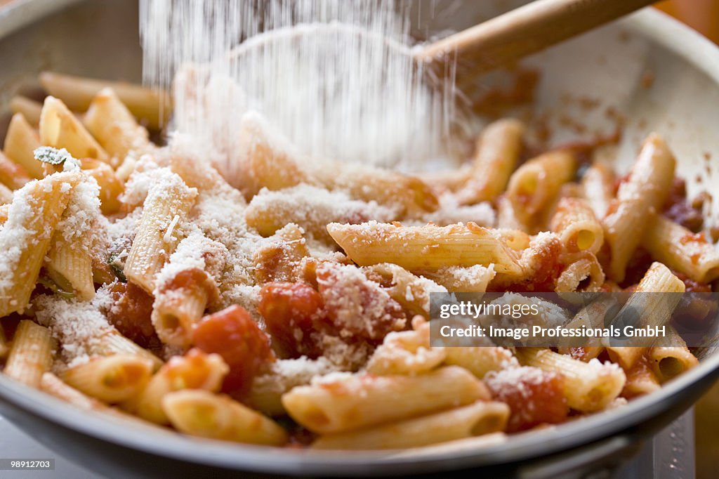 Pouring parmesan cheese to penne with tomato sauce in saute pan, close-up