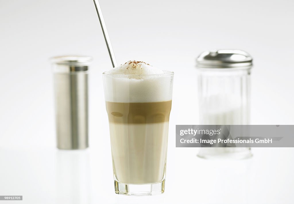 Glass of latte macchiato with sugar and cocoa shakers, close-up