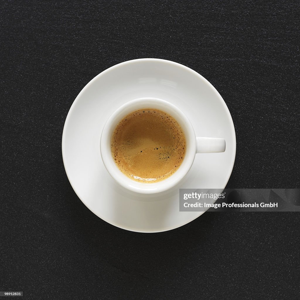 Cup of espresso on black background, overhead view, close-up