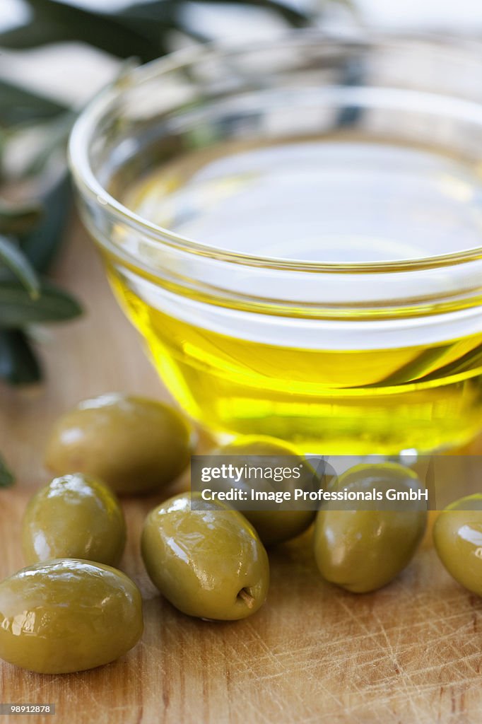 Green olives and bowl of olive oil, close-up