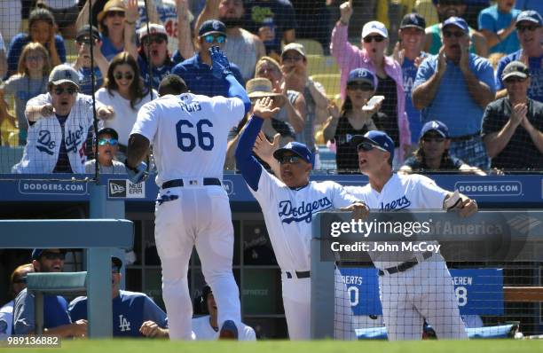 Yasiel Puig of the Los Angeles Dodgers is welcomed into the dugout by Manager Dave Roberts and Bob Geren after scoring a run in the eighth inning...