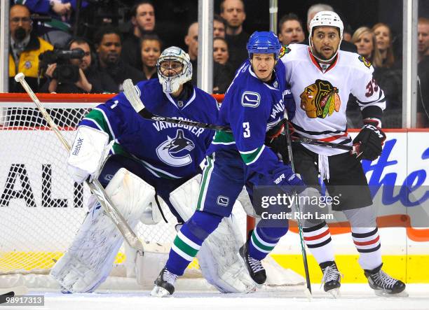 Goalie Roberto Luongo of the Vancouver Canucks tries to keep his eye on the puck while teammate Kevin Bieksa tries to clear Dustin Byfuglien of the...