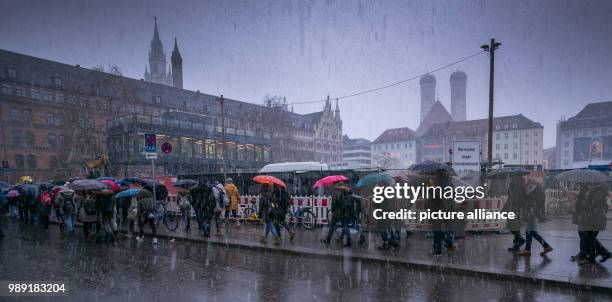 Passers-by carrying umbrellas walking under heavy snow fall in front of the scenery provided by the City Hall and the two towers of the Frauenkirche...