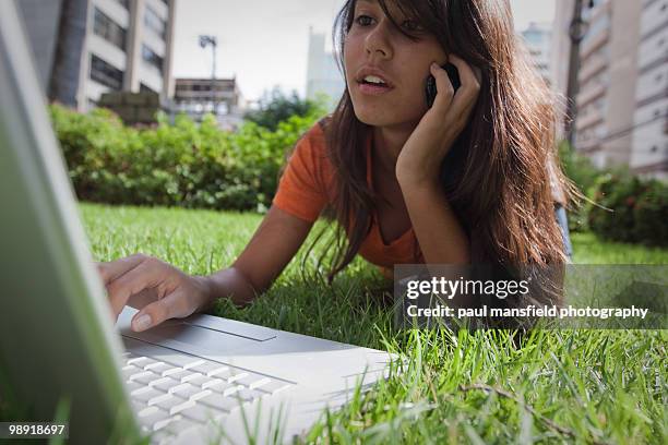 teenage girls using laptop and phone in park - paul mansfield photography stock pictures, royalty-free photos & images