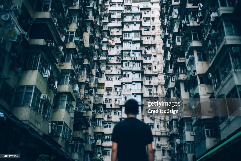 Rear view of young man surrounded by old traditional residential buildings and lost in city