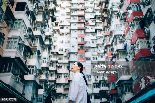 low angle view of woman surrounded by old traditional residential buildings and looking up to sky in city - solo 2018 film foto e immagini stock