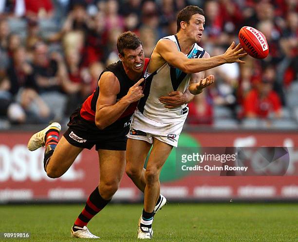 Travis Boak of the Power handballs whilst being tackled by David Hille of the Bombers during the round seven AFL match between the Essendon Bombers...